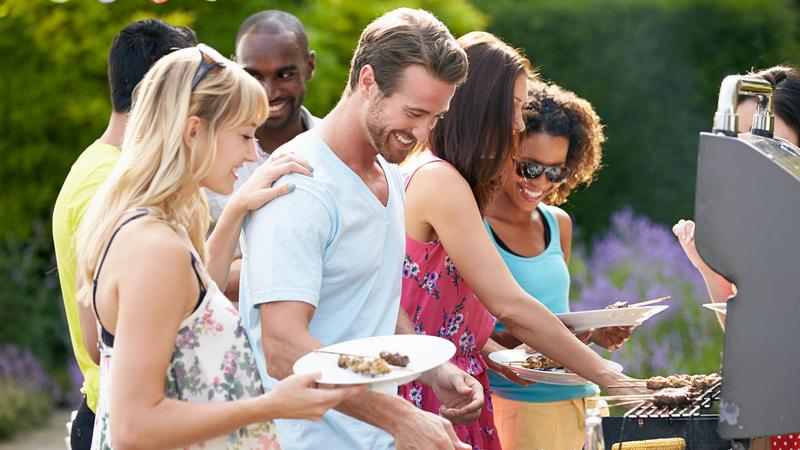 Group Of Friends Having Outdoor Barbeque At Home In Garden
