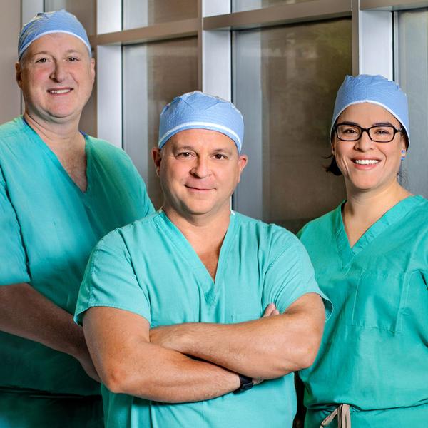 A group of bariatric surgeons, wearing green scrubs, poses for a photo in a hospital hallway.