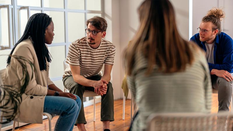 A group of young adults participates in a group therapy session in an office setting.