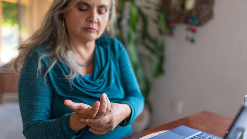 A woman massages her aching hand while sitting at a desk in front of her laptop.