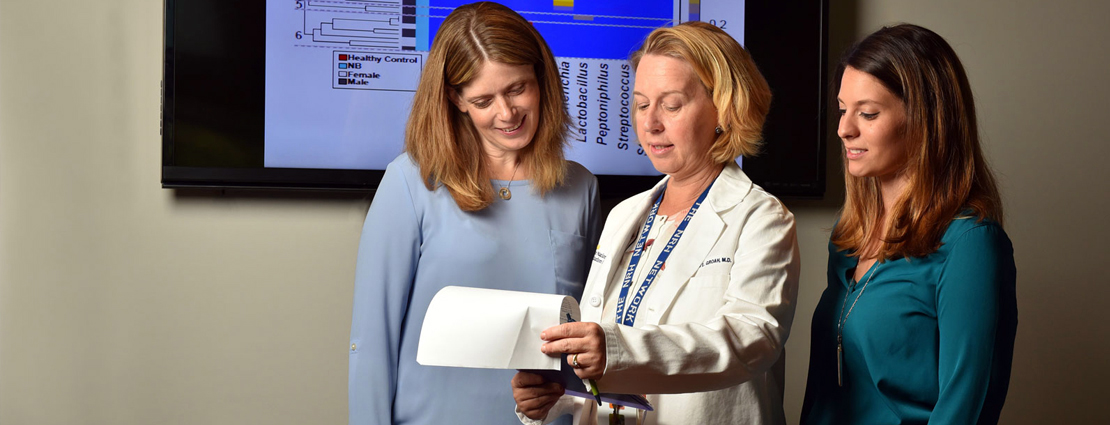 Three female medical professionals look over some papers while standing in a hospital hallway.