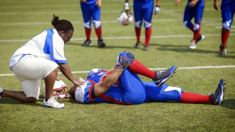 An athletic trainer helps a football player who is laying on the ground during a game.