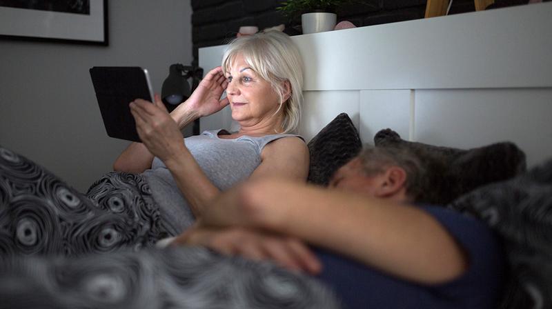 A woman uses an ipad in bed because she has insomnia.