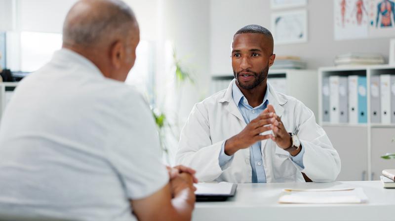 A doctor talks with a patient in an office setting.