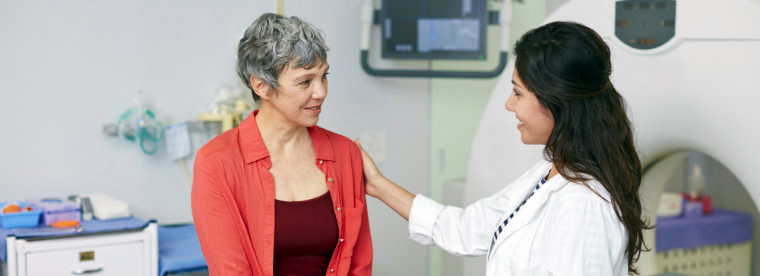 A woman, wearing a red shirt, talks with her doctor in a medical office setting.