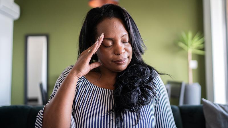 A woman holds a hand to her forehead in pain.