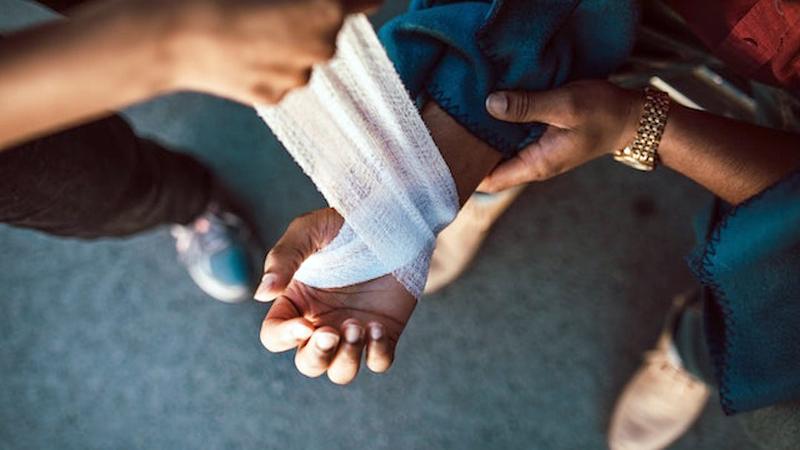 Close up photo of a person's hand being bandaged by a care-giver.