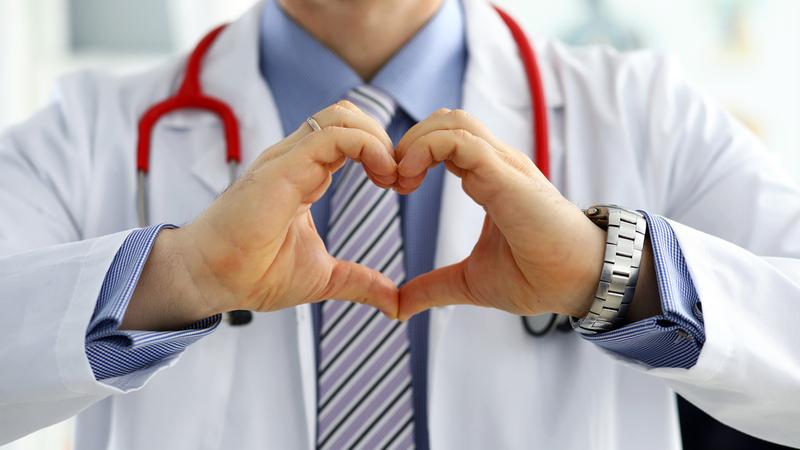 Close up photo of a doctor making a heart symbol with his hands.
