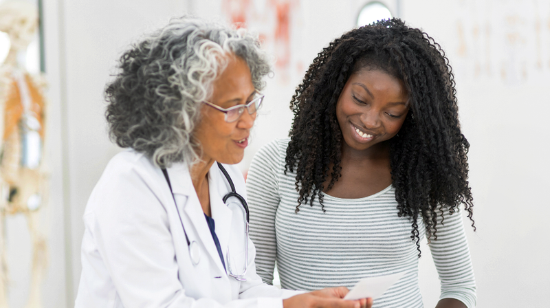 A female doctor talks with a patient in a clinical setting.