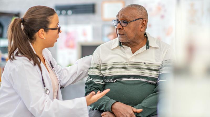 A doctor crouches down to speak with a patient who is sitting in a chair.