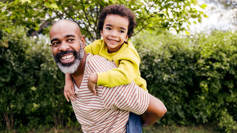 A young boy gets a piggyback ride while playing outside with his father.