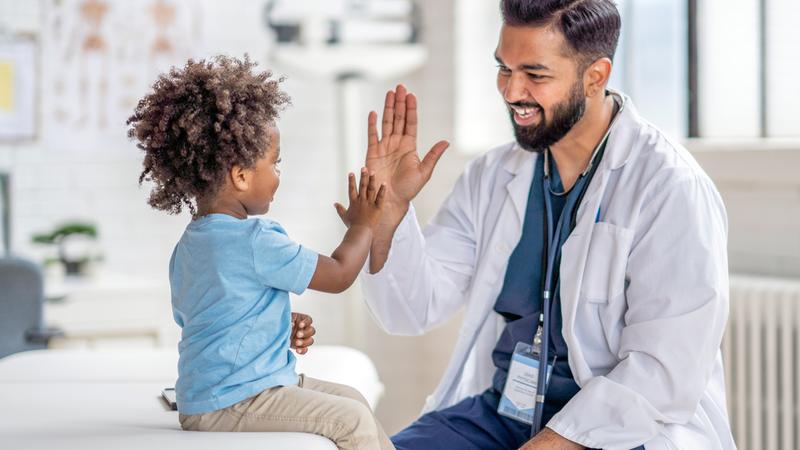 A doctor gives a high-five to a child patient in a clinical setting.