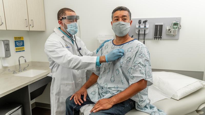 A doctor listens to a patient's heart during an office visit. Both people are wearing masks.