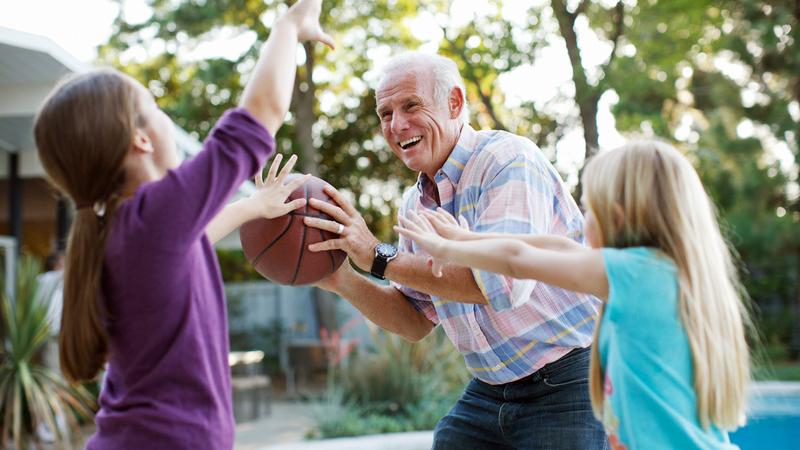 A senior man plays basketball with his grandchildren.