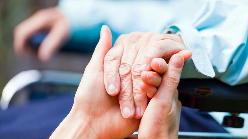 Close up photo of younger hands holding and elderly person's hands.