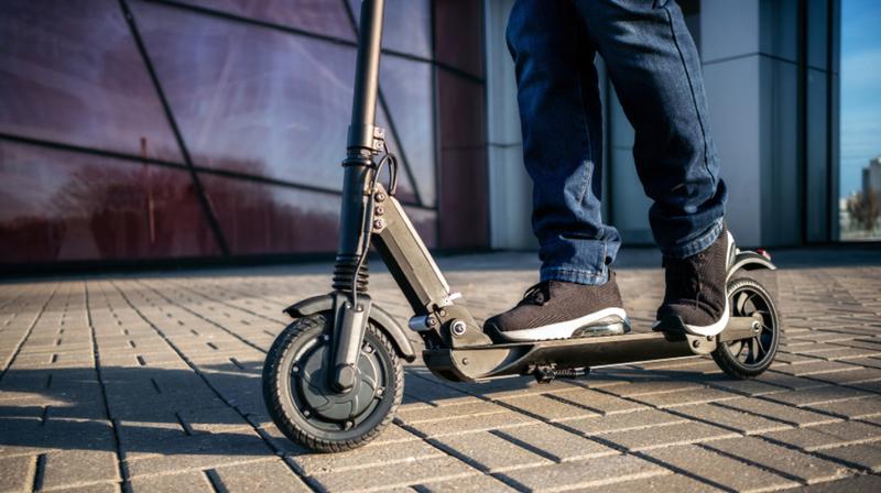 Close up of a person riding an electric scooter in an urban setting.