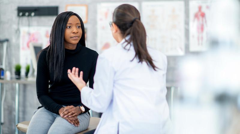 An african american female patient talks to her doctor in a clinical setting.