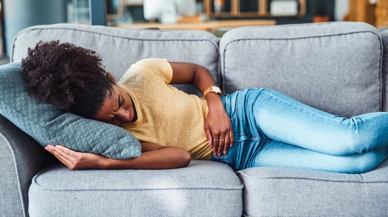  A young woman experiencing stomach pain while lying on the sofa at home.