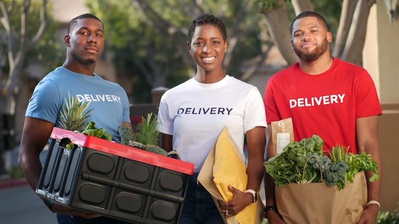 A team of 3 people hold groceries and packages during a delivery route.