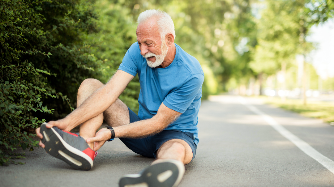 A senior man holds his ankle after injuring it while running in the park.