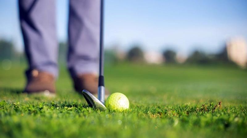 Close up photo of a golfer holding a golf club next to a ball, ready to hit a shot on a golf course.
