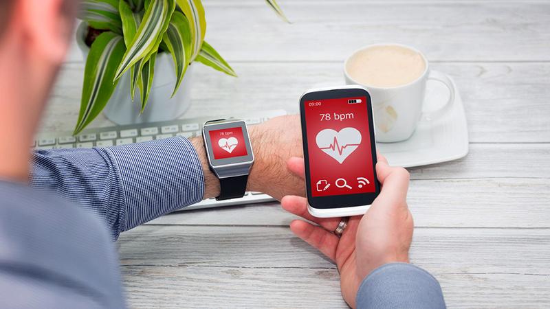 A man wears a heart health monitoring device and looks at the corresponding app on his cell phone.