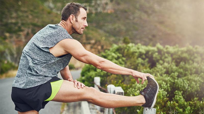 A man stretches his leg during a run in an outdoor setting.