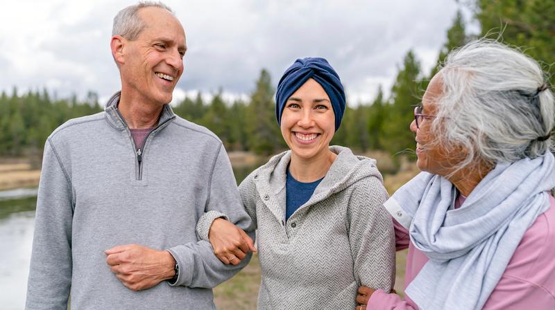 Portrait of a woman wearing a head scarf smiling directly at the camera while spending time outdoors with her parents. 