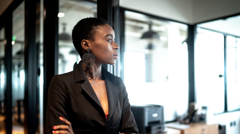 An african american business woman stands with her arms crossed.