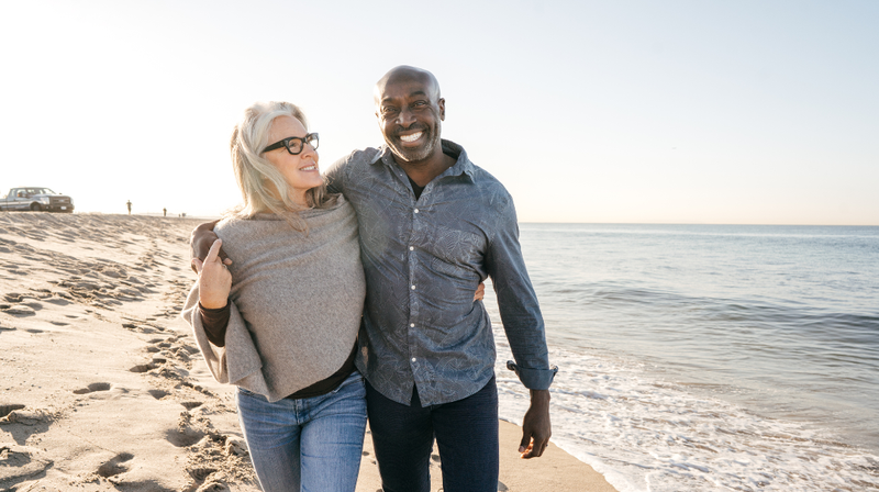 A couple walks together on a beach near the water.