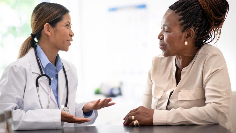 A doctor talks with a middle-aged woman in a clinical setting.