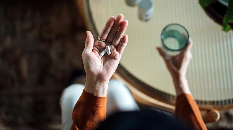 Close up photo from a high angle of a hand holding pills and a cup of water.