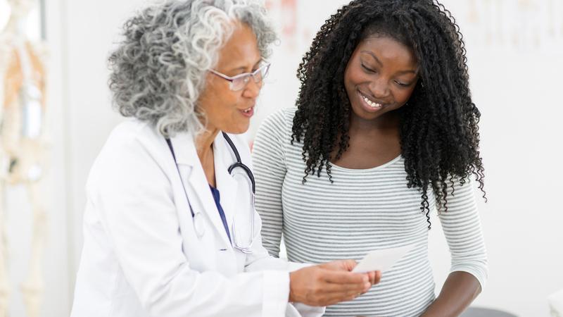 A senior female doctor talks with a young female patient in a clinical setting.