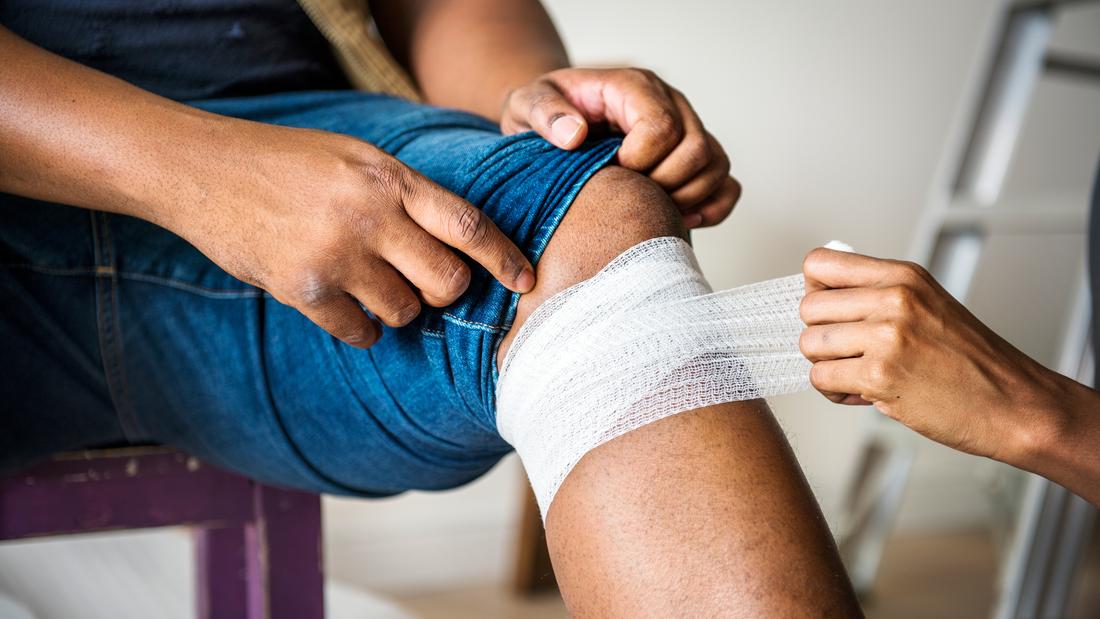 Close up photo of a nurse applying a bandage to a person's knee.