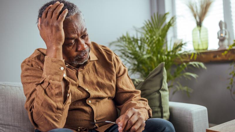 An elderly african american man sits on his sofa at home.