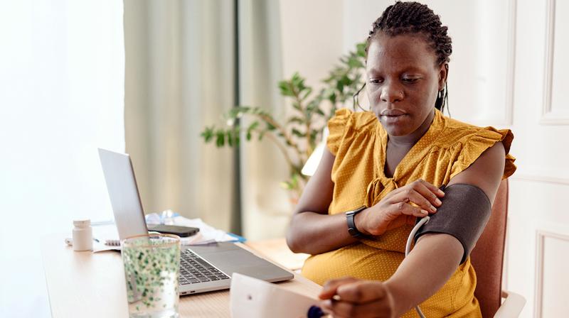 A young african american mother takes her blood pressure reading in her home.