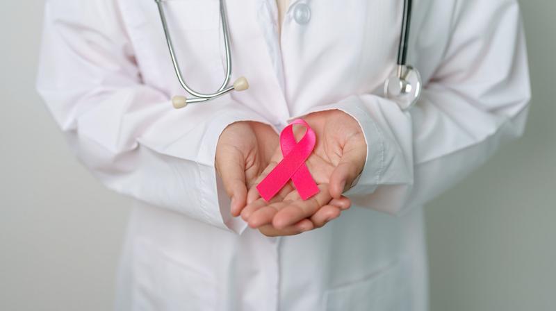 Close up photo of a doctor holding a pink ribbon in their hands.