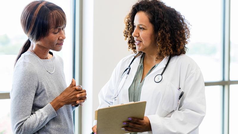 A female patient and her doctor stand together as they discuss the test results on the clipboard held by the doctor.