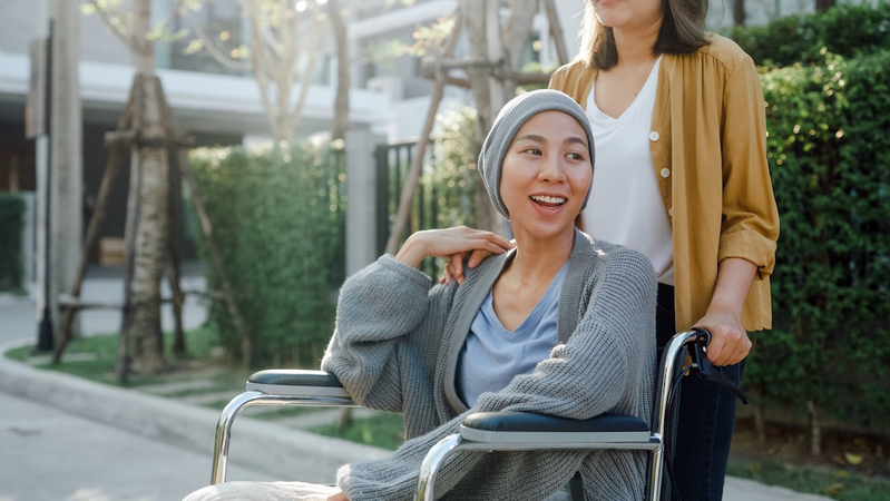 A young woman wearing a head scarf sits in a wheelchair outoors.