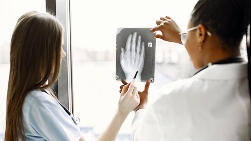 2 doctors look at an xray film in front of a window.