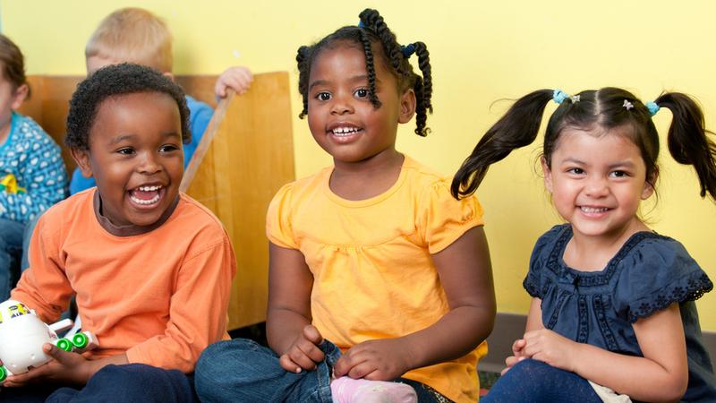 A group of children smiles and laughs in an early childhood education setting.