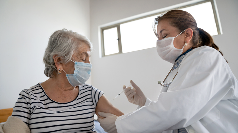 A doctor gives a vaccination shot to a mature female patient in a doctor's office.