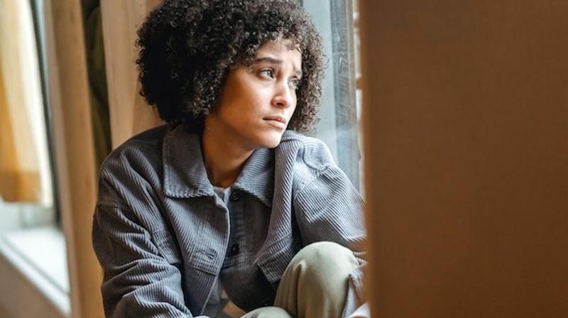 A young woman sits on a window ledge and looks out.