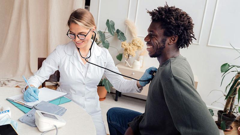 A doctor listens to a patient's heart while jotting down notes during an office visit.