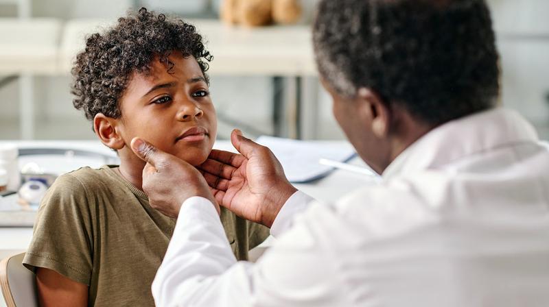 A doctor examines a young boy's neck during an office visit.