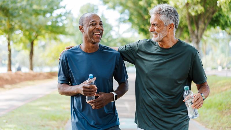 Two men talk as they walk together on a park path outdoors.