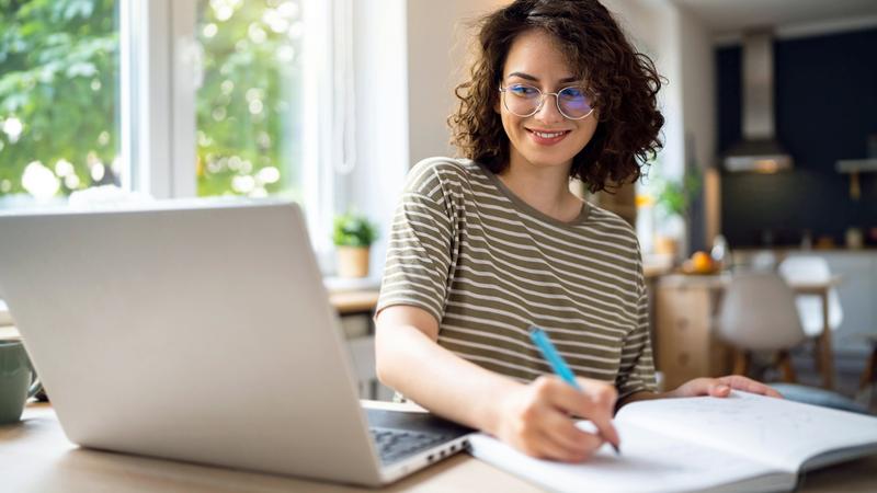 A woman looks at her laptop computer while taking notes.