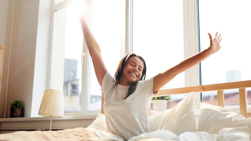 A woman stretches after waking up from a restful sleep.