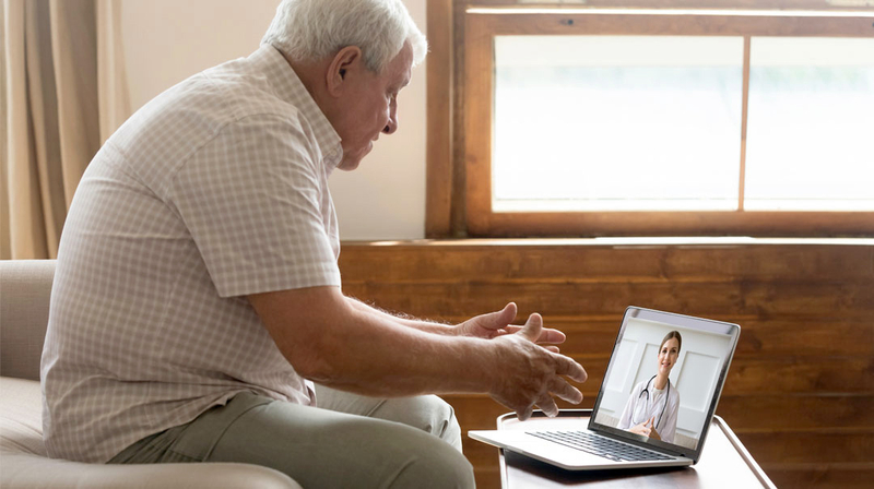 A senior man talks with his doctor on a laptop computer during a telehealth visit.