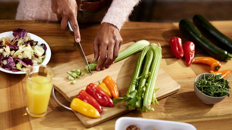 Close up photo of a woman cutting fresh fruits and vegetables.